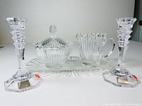 Front angle showing creamer, sugar bowl with lid on rectangular underplate, and pair of candlesticks arranged symmetrically.