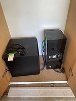 Two black Pinnacle speaker units placed inside a wooden cabinet, one smaller main speaker and one larger subwoofer with visible rear connections and cables.