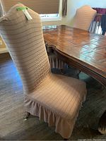 Side view of a wooden dining chair with beige fabric slipcover and skirting, showing the overall appearance and condition.