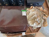 Box containing the glass vase and plates wrapped in brown packing paper shown unopened.