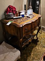 Side view of the granite top wood side table showing curved legs, ornate carving on wood base, and worn condition.