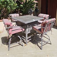 Square outdoor table with stone tile top and 4 matching swivel chairs with striped cushions, showing one missing tile on the table and general dirt accumulation.