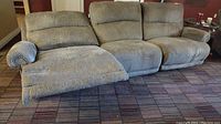 Three seat electric reclining couch sectional with beige fabric upholstery, shown with one seat reclined.