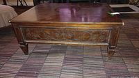 Front view of rectangular wood coffee table with ornate floral and scrollwork carvings on the front apron and tapered legs