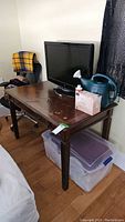 Wood desk with objects on top and storage container underneath, showing overall condition and environment.