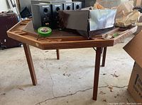 Photo showing overall view of the wooden octagonal poker table with four legs, items placed on top including tape and speakers.