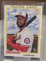 Front of 2022 Lucius Fox baseball rookie card showing player in Nationals uniform with bat and baseball field background.