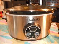 Photo showing front digital control panel of Beaumark crock pot on a colorful cloth surface with wooden furniture in background.