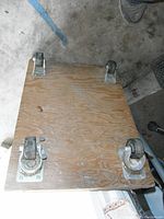 Top view of wooden dolly showing attached caster wheels, including two locking wheels and two swivel wheels, on a concrete floor.