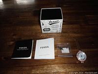Lot contents including Fossil smartwatch, instruction manuals, original box, and extra watch links on wooden surface.
