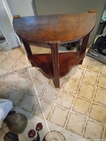 Side angled view of the wooden half moon table showing curved top and two legs with lower shelf below.