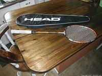 BADMINTON racket with white grip and accompanying black protective HEAD case displayed on wooden table