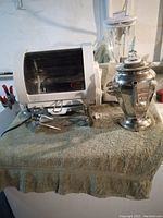 George Foreman rotisserie oven, Oster blender, and vintage coffee maker arranged on a surface covered by a towel.
