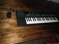 Full view of Yamaha keyboard with power adapter showing black casing, keyboard keys, and cable