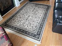 Full view of the rectangular area rug placed on a wooden floor near furniture, showing the main visible pattern and overall condition.