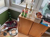 Wide view showing candleholders on window ledge and small table, including green glass boot-shaped candleholders, metal twist candleholders, and additional votive and hurricane-style holders.