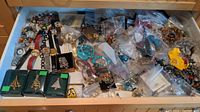 Drawer filled with assorted costume jewelry including watches, brooches, necklaces, bracelets, and earrings seen in a collection