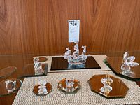 Front view of seven crystal figurines displayed on mirrored glass bases with a MaxSold tag visible.