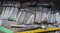 Full view of assorted forks, knives, spoons, and ladle with detailed decorative handles. Shows size relative to measuring tape.