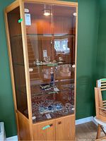 Front view of wood and glass display cabinet showing glass shelves, beveled glass doors, interior light, and wood finish with visible grain and scratches.