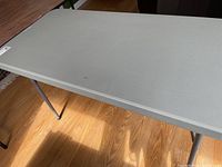 Full view of the rectangular gray resin folding table on a hardwood floor, legs extended.
