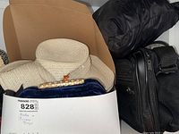 Photo of two woven straw hats, black velvet purse with floral clasp, and black puffer style bag in a box