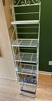 Full view of the large decorative metal shelf unit showing four slatted shelves and detailed scrollwork on the side and top