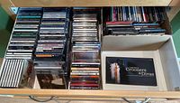 Drawer with multiple rows of assorted music CDs, various artists and genres mostly in jewel cases.