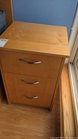 Front view of the night table showing three drawers with curved metal handles.