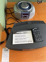 Bose Wave system with remote control and warranty pamphlet beside a portable CD player on an orange table.