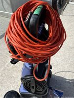 Pressure washer unit with orange extension cord coiled on top and black hose coiled below, showing front and side view.
