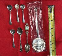 Seven sterling silver spoons displayed on red background, showing variety of shapes and styles including two smaller mustard spoons and decorative spoons.