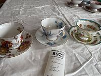 Three sets of Royal Albert tea cups and saucers displayed on a white fabric surface, showing various floral and fruit designs with gold accents.