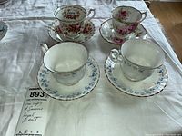 Four sets of porcelain Royal Albert teacups and saucers displayed on a cloth. Floral patterns with gold trim visible. Crazing noted.