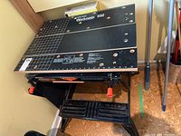 Front view of the Black & Decker Workmate 550 showing wooden top boards with holes and black metal frame with orange clamp handles.