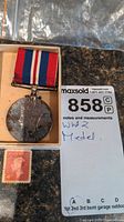 Full medal with attached red, white, and blue ribbon next to Canadian vintage stamp in a box.