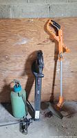 Full view of the lot showing the green manual sprayer, black electric leaf blower, and orange battery-operated trimmer.