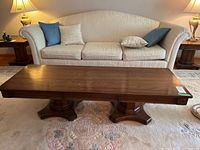 Front view of rectangular wooden coffee table in front of cream upholstered sofa with blue and beige pillows. Shows overall shape and size.