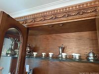 Glass cabinet shelf displaying the metal urn, peltro pitcher, silver plate bowl, espresso cups with saucers, sugar bowl, and plate.