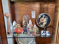 Shelf display with religious Limoges plate, miniature porcelain tea set, and figurines including Delft shoes