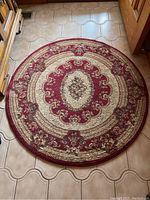 Full view of the round area rug showing the red and beige floral design and its size relative to floor tiles.