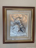 Full view of framed sterling silver relief showing Madonna and child wrapped in cloak with inscription below.
