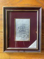 Full view of framed sterling silver relief artwork showing maroon mat and two-tone frame.