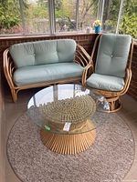 Front view of bamboo loveseat, swivel chair, glass-top table arranged on round rug