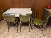 Photo showing retro table with laminate top and five green vinyl chairs arranged around it.