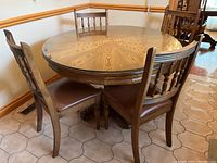 Round wood dining table with clear glass top and surrounding chairs in corner of room