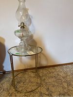 Full view of retro metal frame table with round glass top and clear glass oil lamp sitting on top.