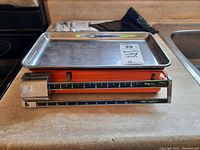 Side view of Terraillon vintage scale showing orange metal body, black measuring scale marked up to 10kg, and stainless steel tray on top.