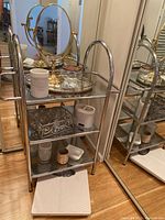 Front angle of metal bathroom shelf with all accessories displayed on shelves including the oval mirror, toothbrush holders, glass jar, soap dish, and bathroom scale.