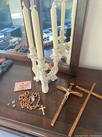 Photo showing wooden crosses, rosary beads, white ceramic candle holder, and candles arranged on a wooden surface in front of a mirror.
